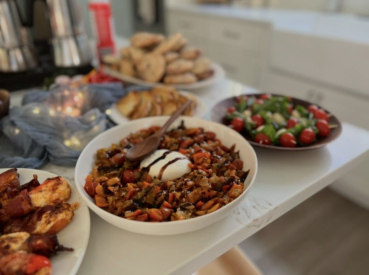 A bowl of roasted peppers and tomatoes topped with burrata and balsamic glaze