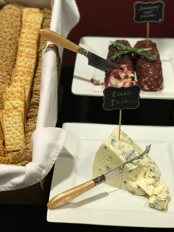 A wedge of blue cheese and a log of cranberry goat cheese with rosemary, beside a basket of crackers