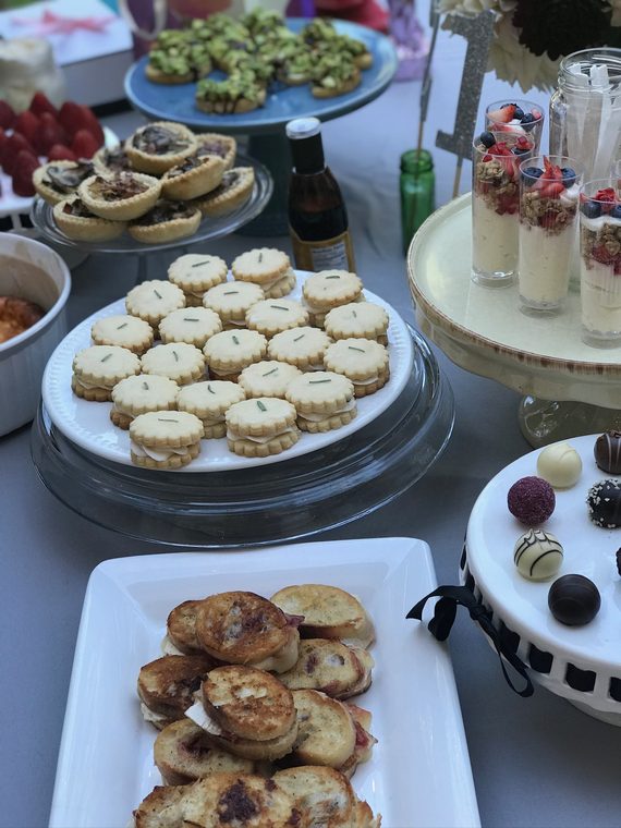 A party table of rosemary shortbread sandwiches, mushroom tartlets, yogurt parfait cups, chocolate truffles and grilled crostini