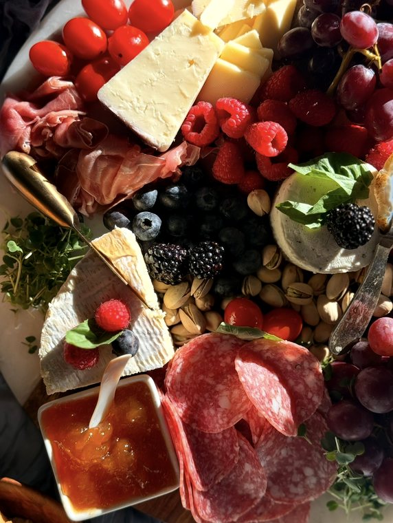 Close-up of a board with prosciutto, salami, aged cheese, brie, berries, pistachios and a dish of apricot jam