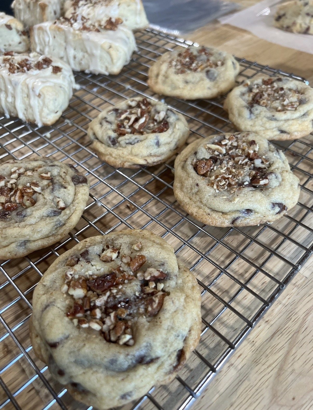 Thick chocolate chip cookies topped with chopped pecans cooling on a wire rack beside maple pecan scones