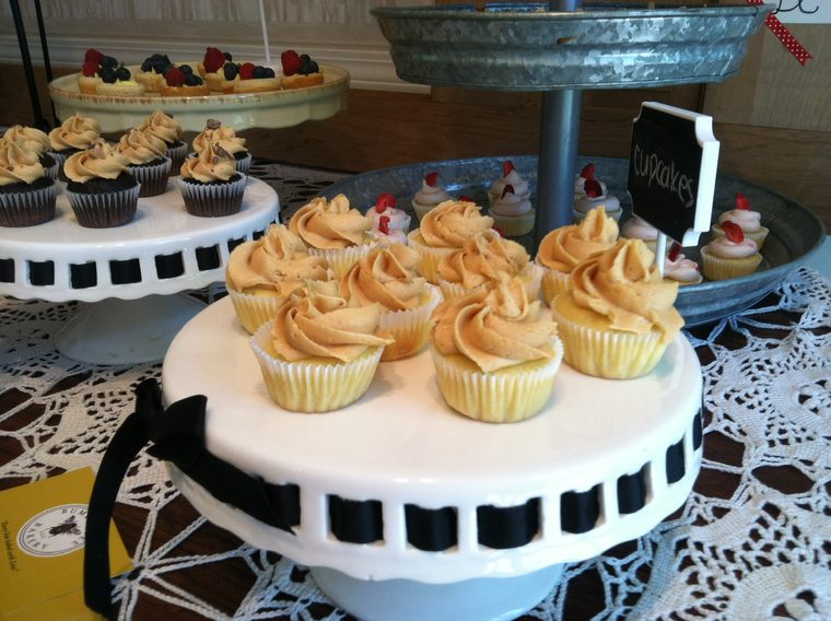 Mini cupcakes with peanut butter buttercream on a cake stand, with fruit tartlets and chocolate cupcakes behind