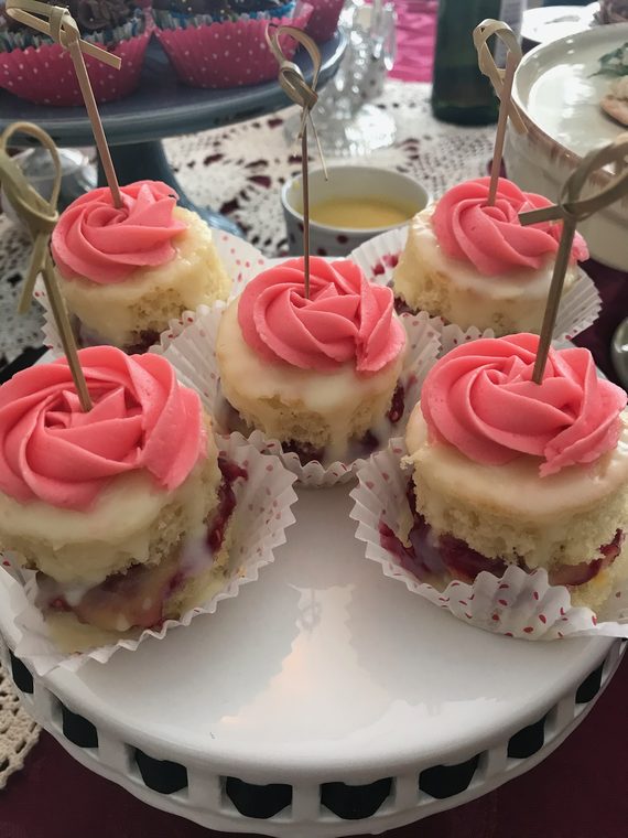 Raspberry-filled vanilla tea cakes topped with pink buttercream roses, each on a knotted pick
