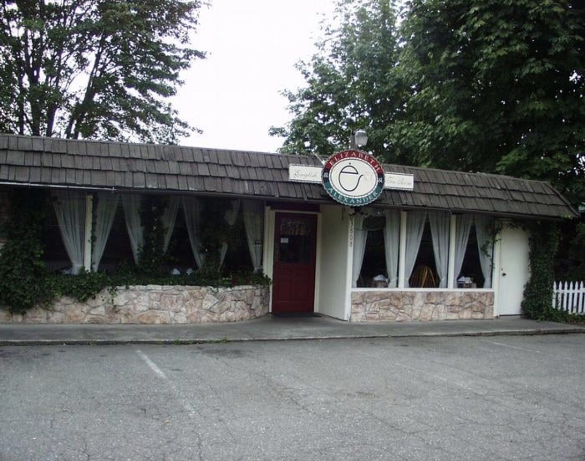 The front of Elizabeth & Alexander’s English Tea Room in Bothell, Washington, with lace curtains, a stone front and a red door