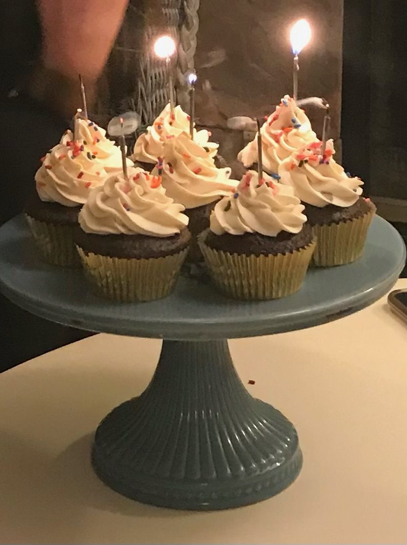 Chocolate cupcakes with swirled vanilla buttercream, sprinkles and lit birthday candles on a blue cake stand