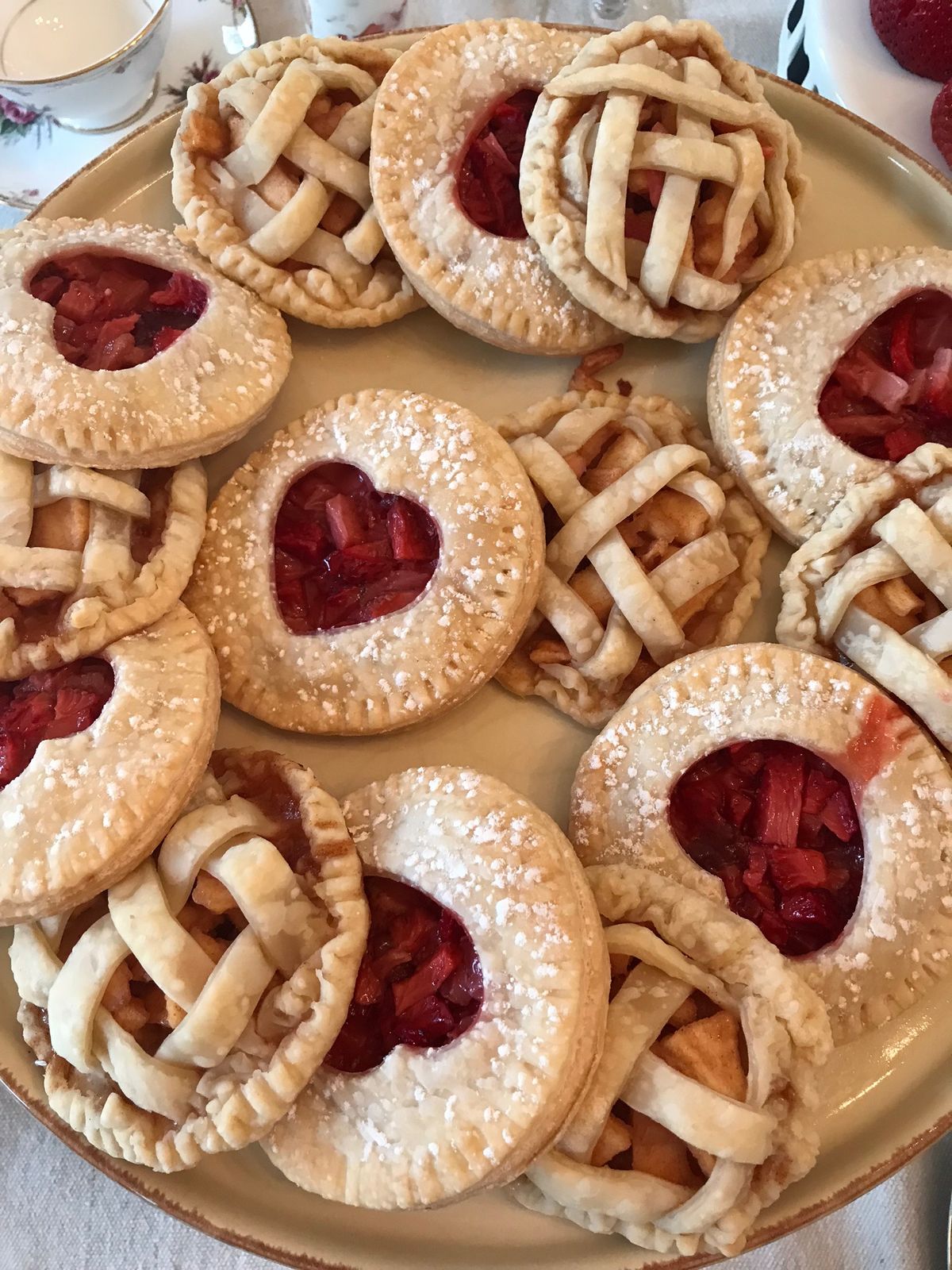 Heart-cut and lattice hand pies on a platter beside a china teacup
