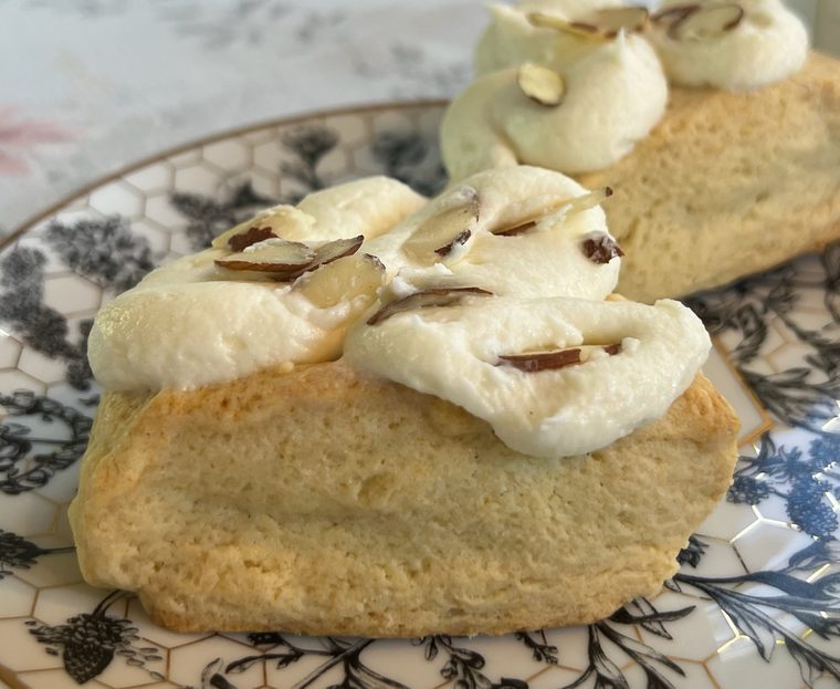 Almond scones topped with almond crème and sliced almonds on a floral honeycomb plate