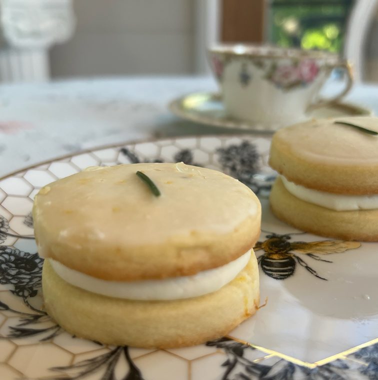 Lemon rosemary shortbread sandwiched with lemon crème on a honeycomb bee plate, with a teacup behind